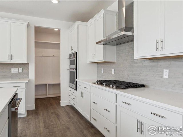 kitchen with wall chimney exhaust hood, appliances with stainless steel finishes, light countertops, white cabinetry, and recessed lighting