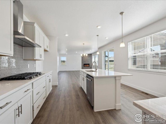 kitchen featuring appliances with stainless steel finishes, a sink, dark wood-type flooring, baseboards, and wall chimney exhaust hood