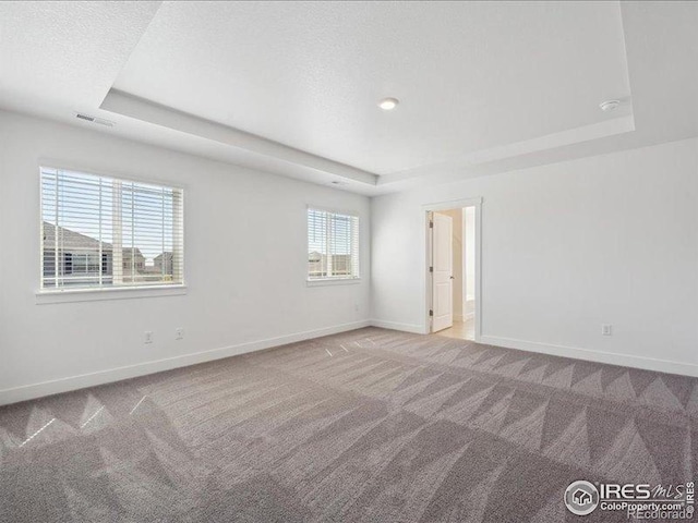 spare room with a tray ceiling, carpet floors, and baseboards