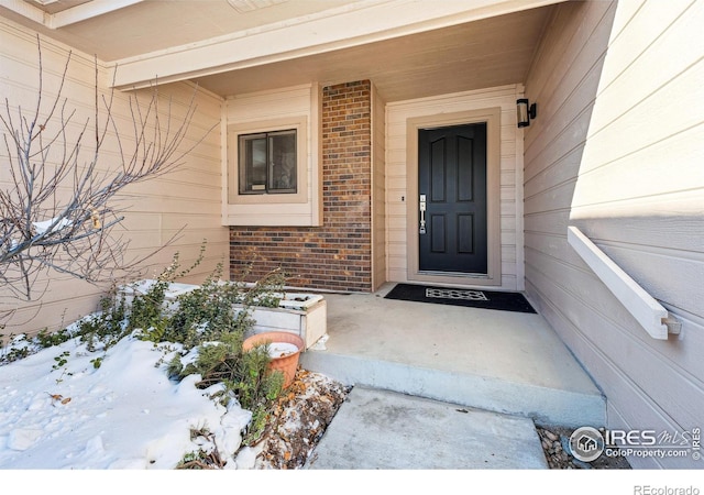 snow covered property entrance featuring brick siding