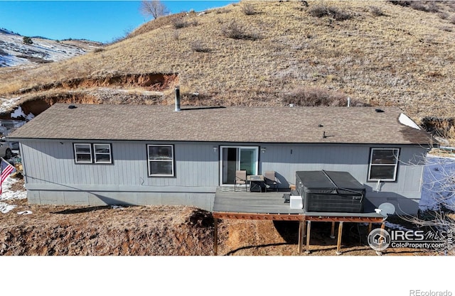 rear view of house with a hot tub and a deck with mountain view