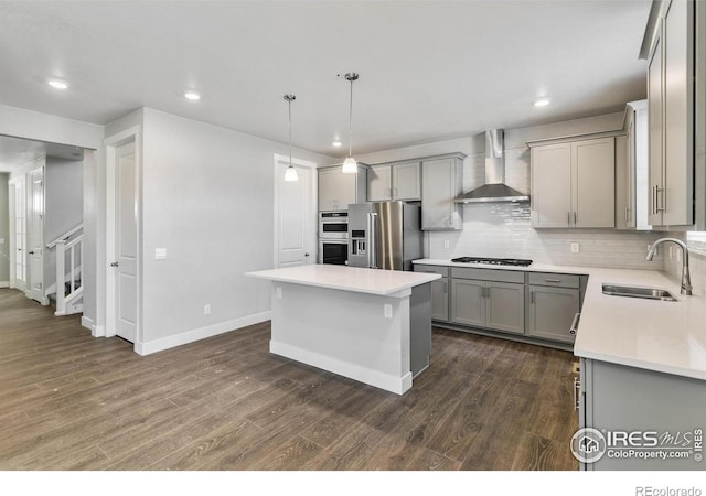 kitchen featuring pendant lighting, sink, appliances with stainless steel finishes, a kitchen island, and wall chimney exhaust hood