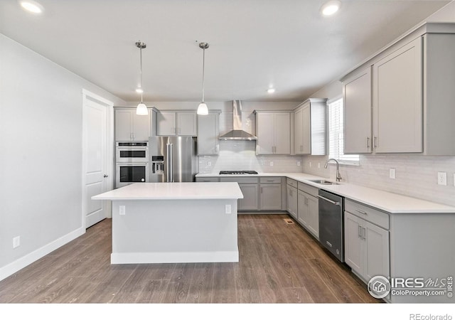 kitchen featuring gray cabinets, appliances with stainless steel finishes, decorative light fixtures, sink, and wall chimney range hood