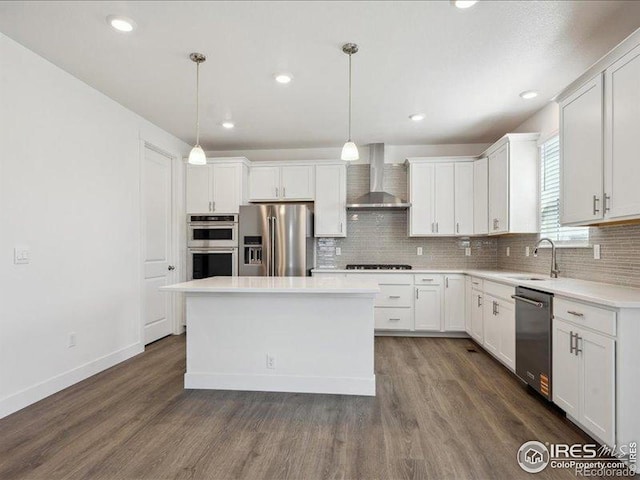kitchen featuring appliances with stainless steel finishes, wall chimney range hood, a sink, white cabinets, and recessed lighting
