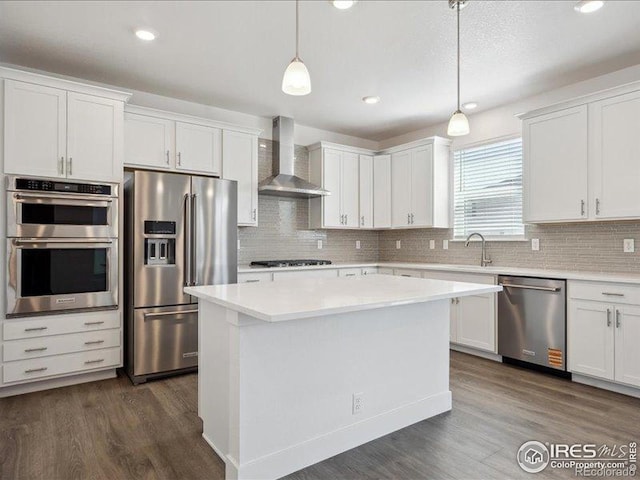 kitchen with appliances with stainless steel finishes, wall chimney range hood, dark wood-style flooring, light countertops, and recessed lighting