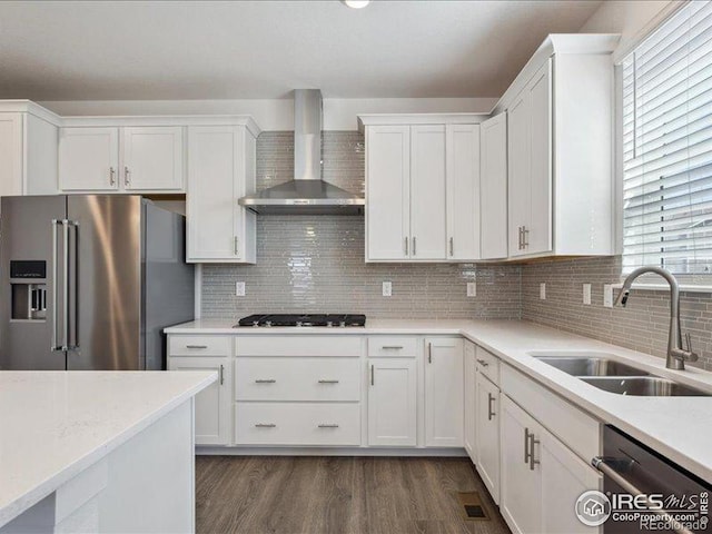 kitchen with stainless steel appliances, wall chimney range hood, a sink, light countertops, and white cabinets