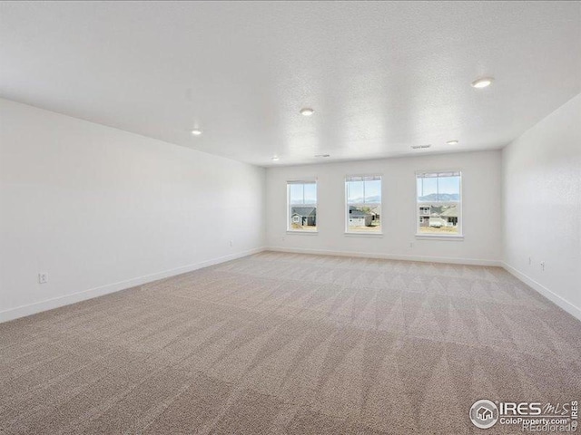 spare room with healthy amount of natural light, light colored carpet, baseboards, and recessed lighting