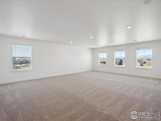 spare room with plenty of natural light, light carpet, baseboards, recessed lighting, and a textured ceiling