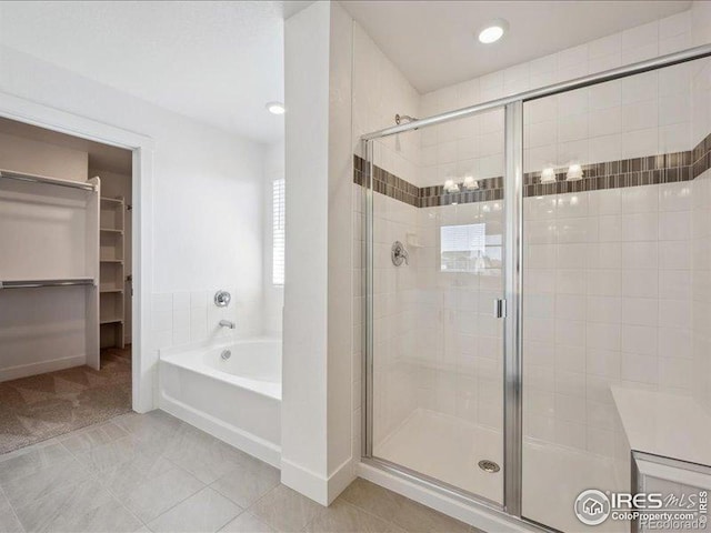 full bathroom featuring a shower stall, a bath, a spacious closet, tile patterned floors, and baseboards