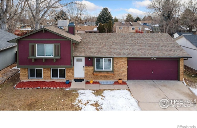 tri-level home with driveway, a shingled roof, an attached garage, and brick siding