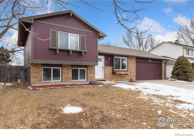 tri-level home with an attached garage, driveway, fence, and brick siding