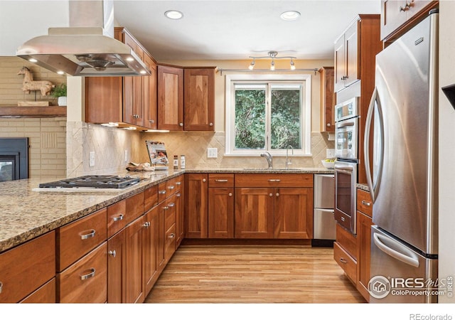 kitchen featuring sink, island exhaust hood, stainless steel appliances, light stone countertops, and light hardwood / wood-style floors