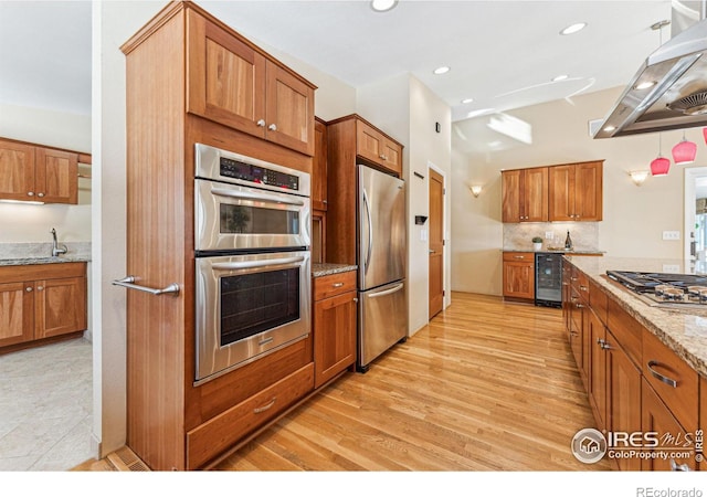 kitchen featuring appliances with stainless steel finishes, wine cooler, island range hood, light stone countertops, and light wood-type flooring