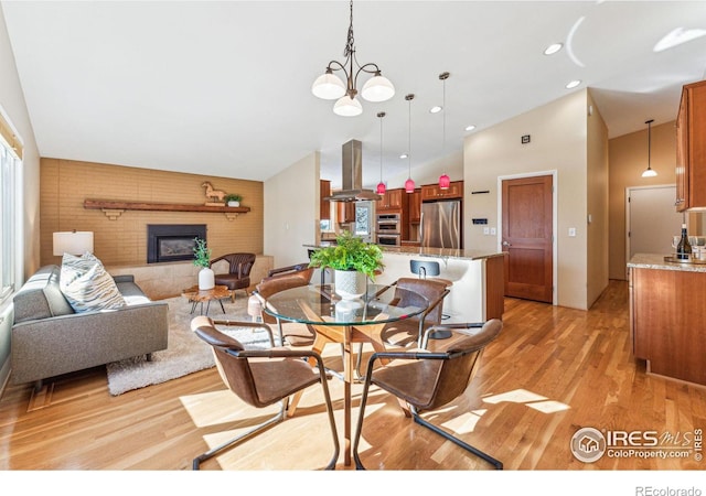 dining room featuring a large fireplace, an inviting chandelier, light wood-type flooring, and a towering ceiling