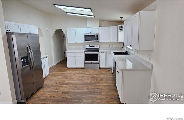 kitchen with white cabinets, dark wood-type flooring, vaulted ceiling, stainless steel appliances, and a sink