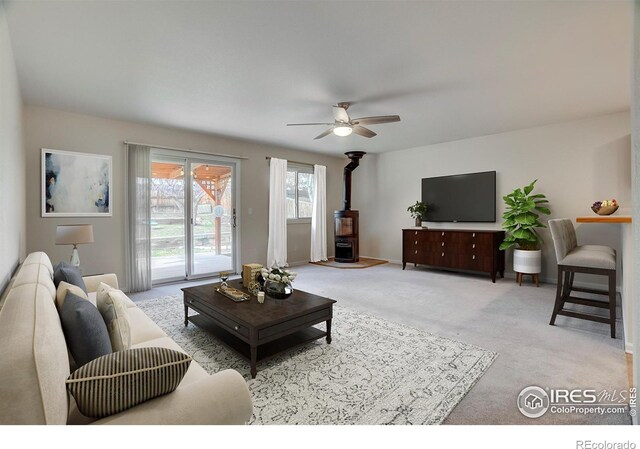living room featuring light colored carpet, ceiling fan, and a wood stove