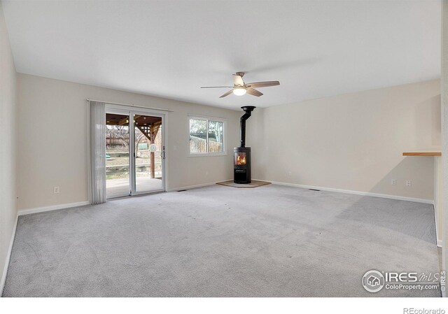 carpeted empty room featuring ceiling fan and a wood stove