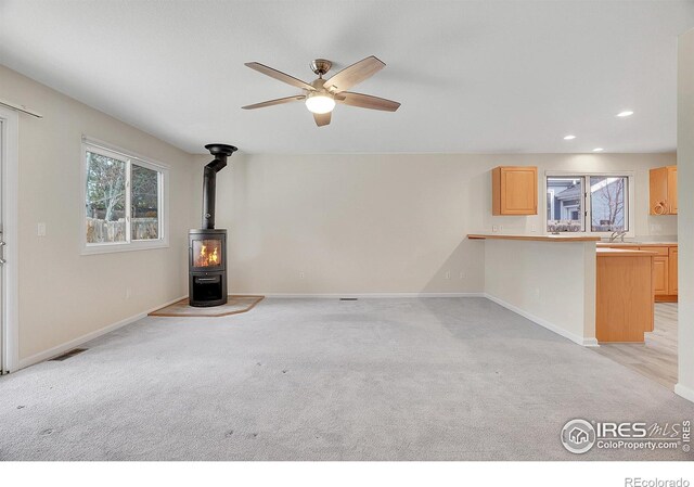 unfurnished living room with a wood stove, light colored carpet, and ceiling fan
