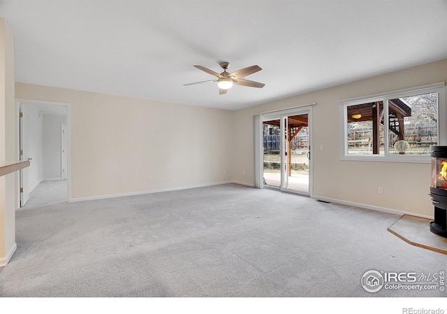 empty room featuring light colored carpet, a healthy amount of sunlight, and a wood stove