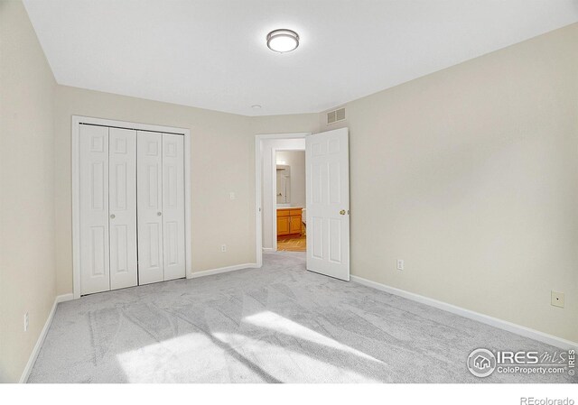 unfurnished bedroom with light colored carpet and a closet