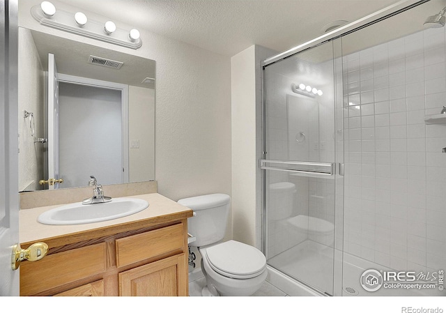 bathroom with vanity, a shower with door, toilet, and a textured ceiling