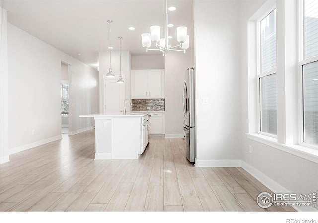 kitchen with a kitchen island with sink, white cabinetry, hanging light fixtures, light countertops, and freestanding refrigerator