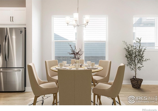 dining space featuring light wood finished floors, baseboards, and a notable chandelier