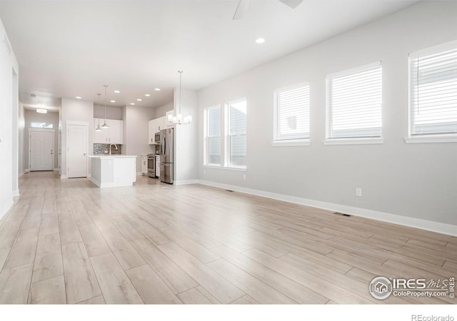 unfurnished living room featuring a wealth of natural light, a sink, and light wood-style flooring