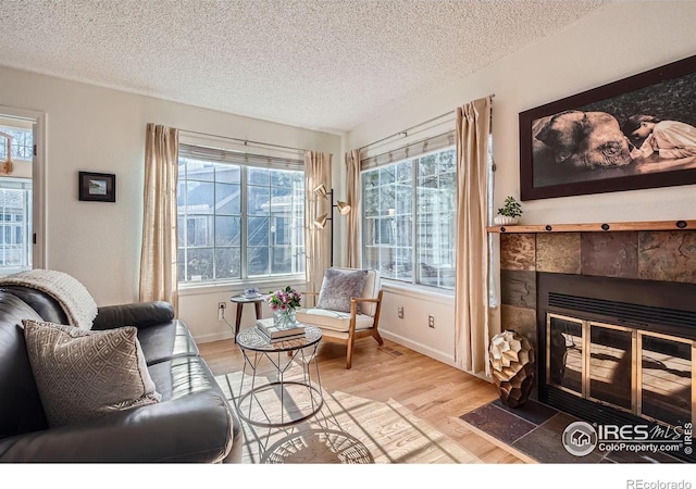 living area featuring a tiled fireplace, a textured ceiling, and light hardwood / wood-style flooring