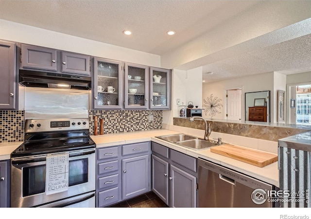 kitchen with sink, dark tile patterned floors, stainless steel appliances, tasteful backsplash, and a textured ceiling