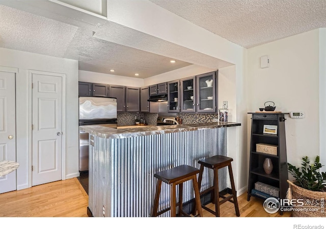 kitchen featuring tasteful backsplash, a breakfast bar, light hardwood / wood-style flooring, and kitchen peninsula