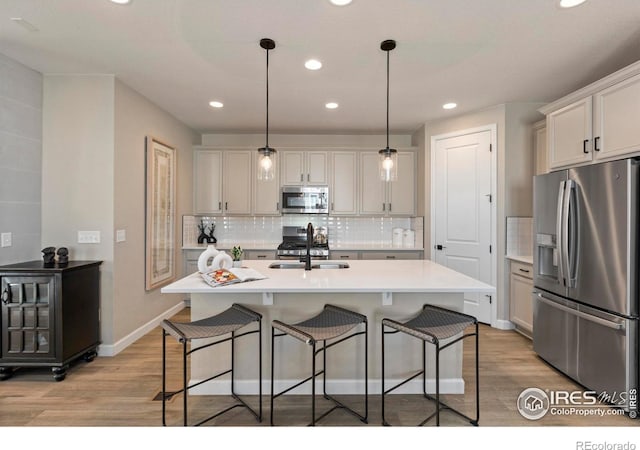 kitchen featuring stainless steel appliances, sink, a center island with sink, and decorative light fixtures