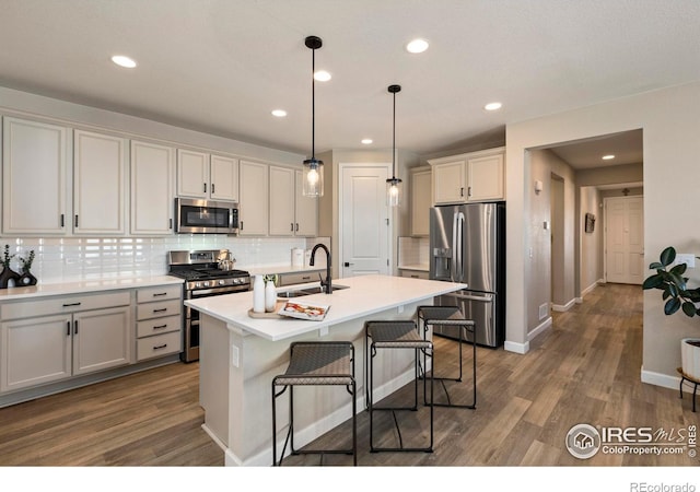 kitchen featuring pendant lighting, sink, a kitchen island with sink, stainless steel appliances, and a kitchen breakfast bar