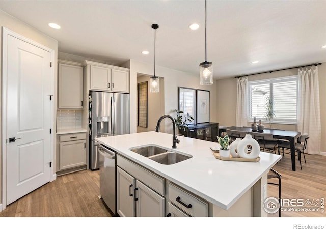 kitchen featuring sink, hanging light fixtures, stainless steel appliances, a center island with sink, and light wood-type flooring