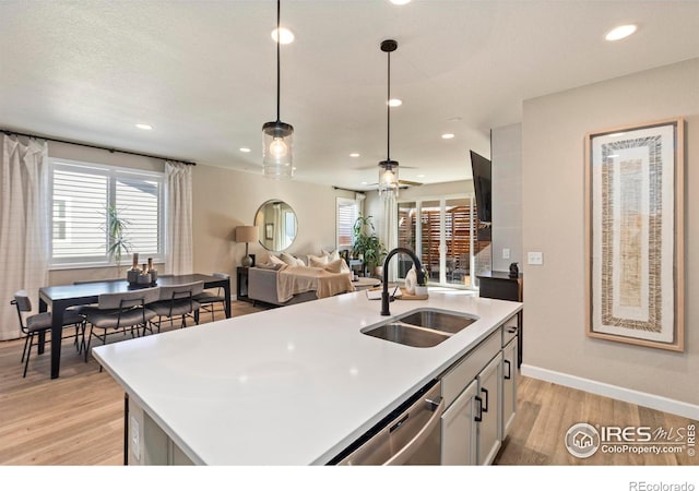 kitchen with sink, a kitchen island with sink, light hardwood / wood-style floors, decorative light fixtures, and stainless steel dishwasher