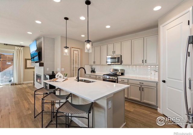 kitchen featuring an island with sink, stainless steel appliances, decorative light fixtures, and sink