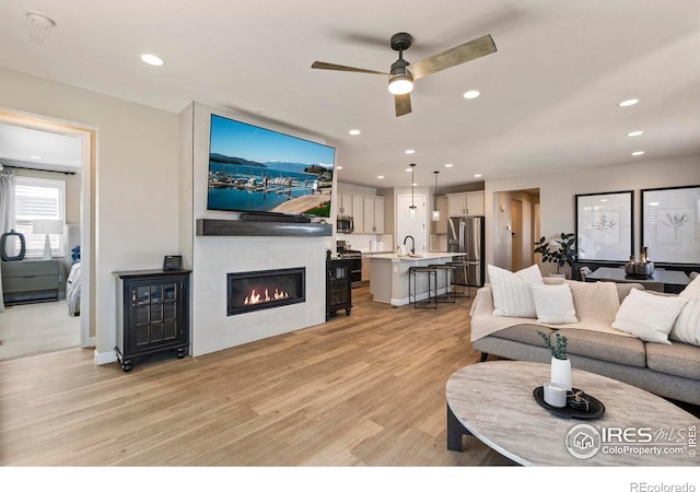 living room featuring ceiling fan, a tiled fireplace, sink, and light hardwood / wood-style flooring