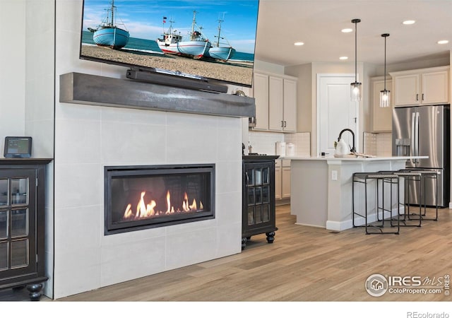 kitchen with stainless steel refrigerator with ice dispenser, hanging light fixtures, light hardwood / wood-style flooring, a kitchen breakfast bar, and an island with sink