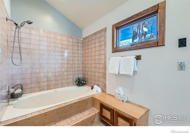 bathroom with tiled tub and lofted ceiling