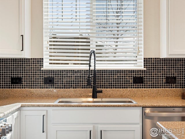 kitchen with sink, backsplash, light stone countertops, white cabinets, and stainless steel dishwasher