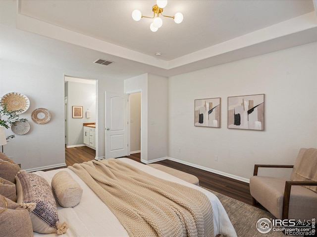 bedroom featuring a raised ceiling, dark wood-type flooring, a chandelier, and ensuite bath