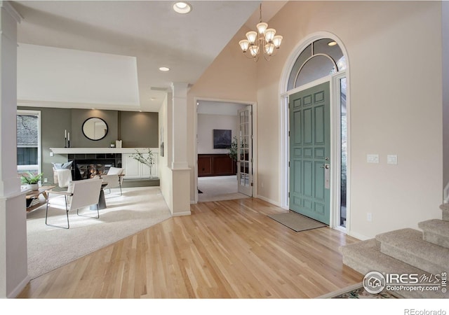 foyer featuring a tiled fireplace, wood-type flooring, a chandelier, and decorative columns