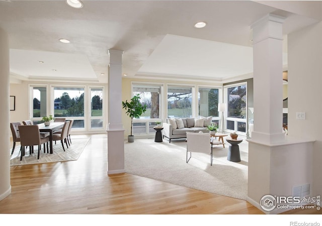 living room featuring ornate columns, light wood-type flooring, and a tray ceiling