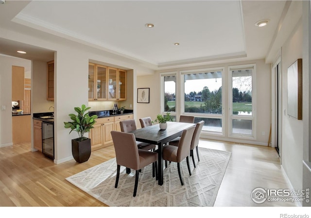 dining room featuring sink, a raised ceiling, and light wood-type flooring