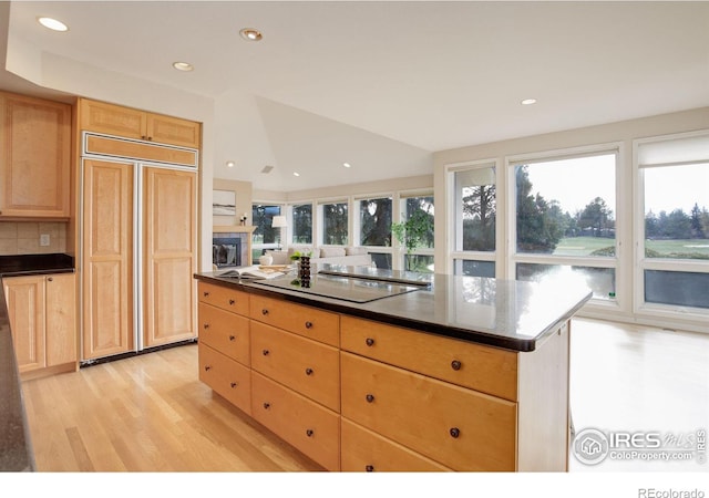 kitchen featuring a kitchen island, light wood-type flooring, decorative backsplash, paneled built in refrigerator, and black electric cooktop