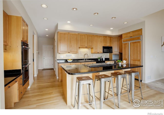 kitchen with tasteful backsplash, a kitchen breakfast bar, a kitchen island with sink, light hardwood / wood-style floors, and black appliances