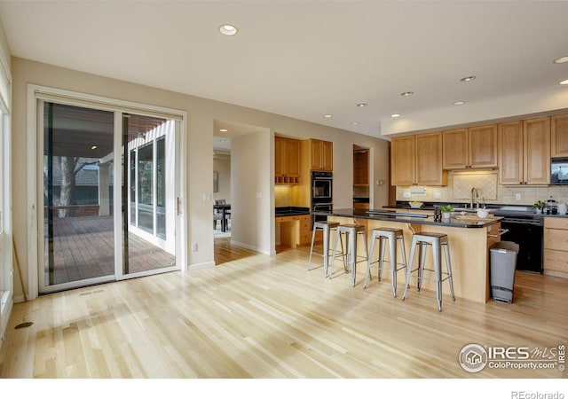 kitchen featuring a kitchen island, tasteful backsplash, black appliances, light hardwood / wood-style floors, and a kitchen bar