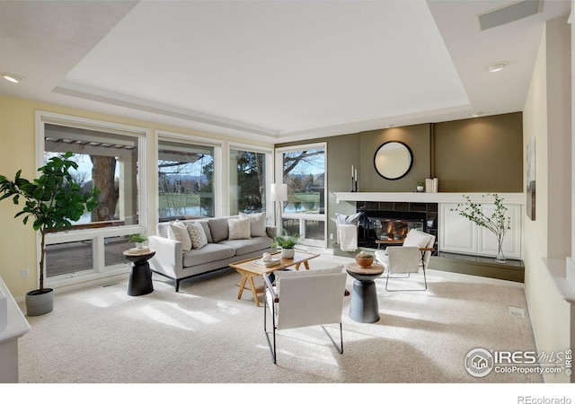 living room featuring a tile fireplace, light colored carpet, and a tray ceiling