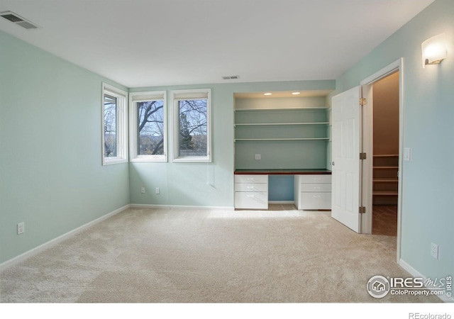 unfurnished bedroom with a walk in closet, built in desk, and light colored carpet