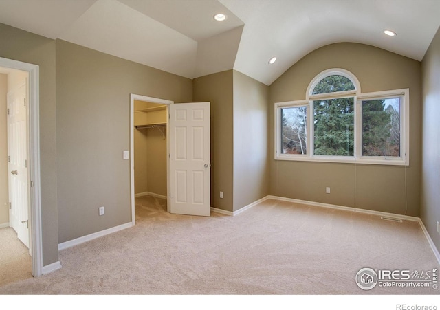 unfurnished bedroom featuring lofted ceiling, a spacious closet, and light carpet